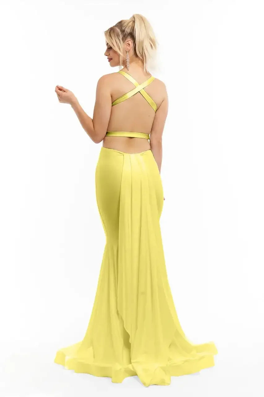 A woman in a vibrant yellow evening gown stands with her back turned, showcasing crisscrossing straps and a flowing skirt, in a plain white background. She gestures gracefully with one hand.