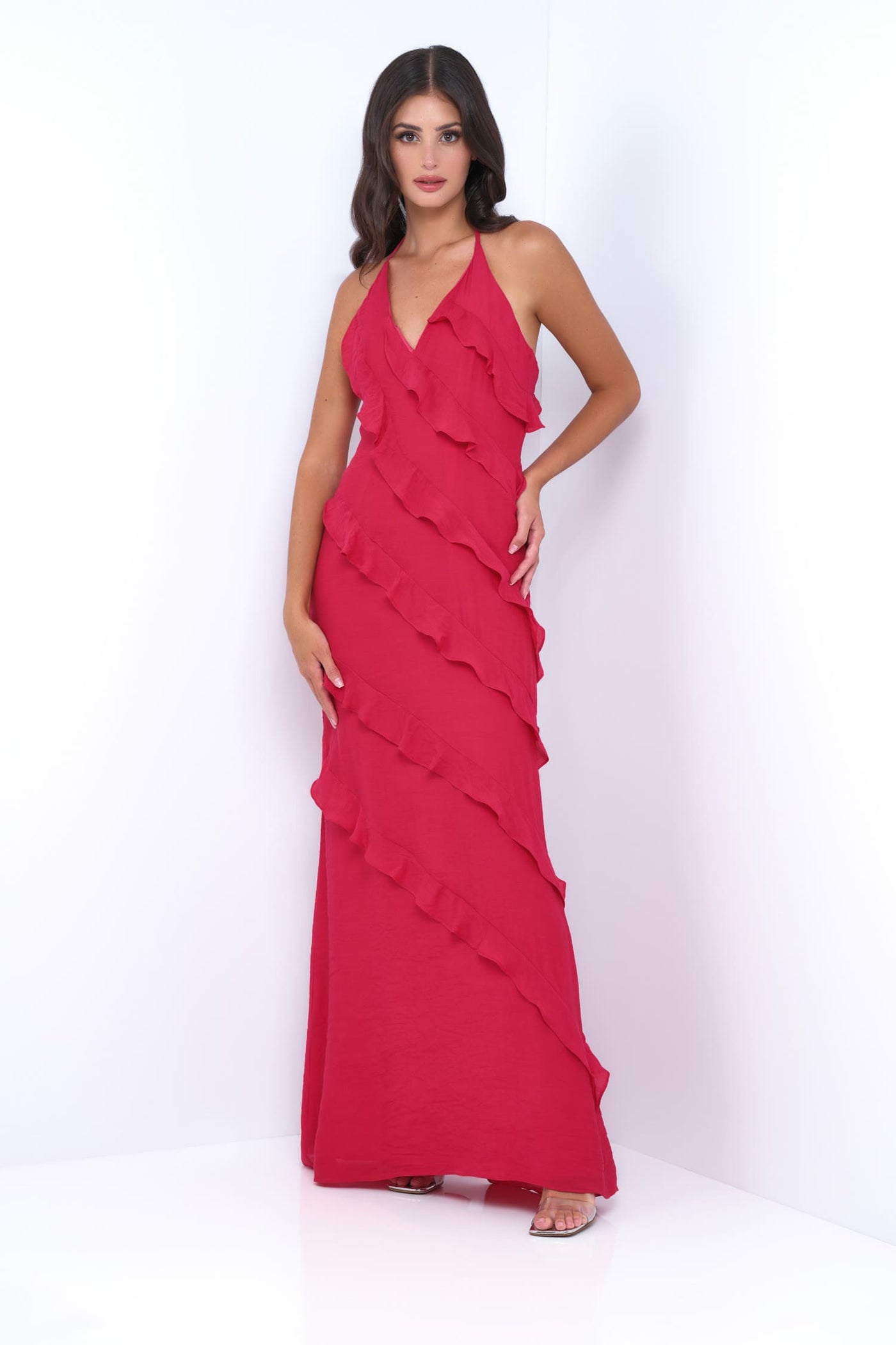 A woman modeling a bright red halter-neck maxi dress with cascading ruffle layers, standing against a clean white studio background.