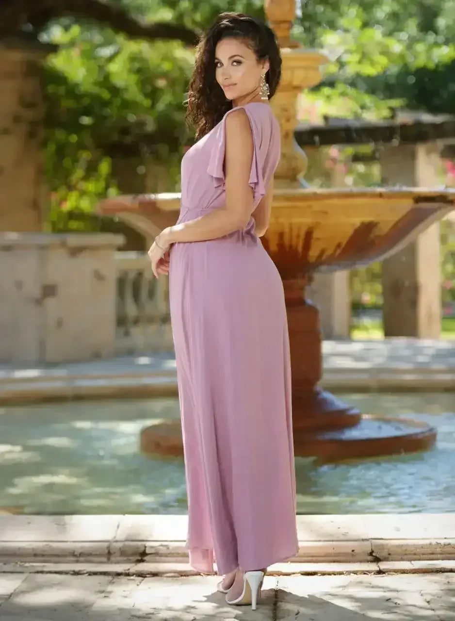 A woman in a flowing, light purple dress stands beside a decorative fountain. She poses confidently with her hand on her hip, set against a lush, green garden backdrop.