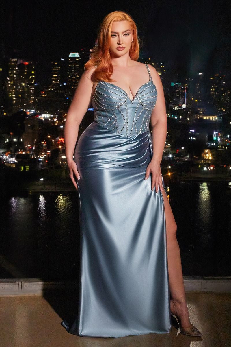 A woman in a shimmering blue evening gown stands confidently, showcasing a high slit. The city skyline glows behind her, indicating a glamorous night setting.