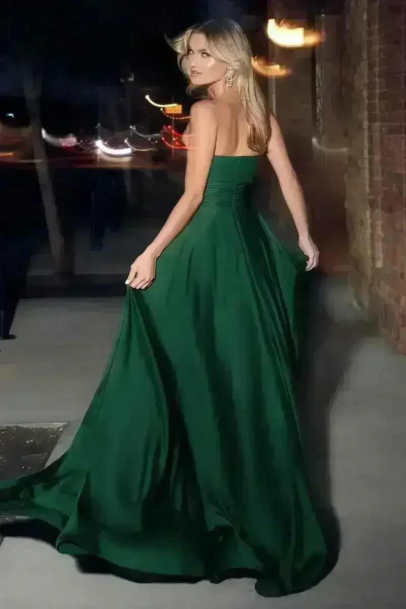A woman in a flowing green gown turns to look back while walking. The setting features subtle outdoor lighting and brick walls, creating an elegant, evening ambiance.