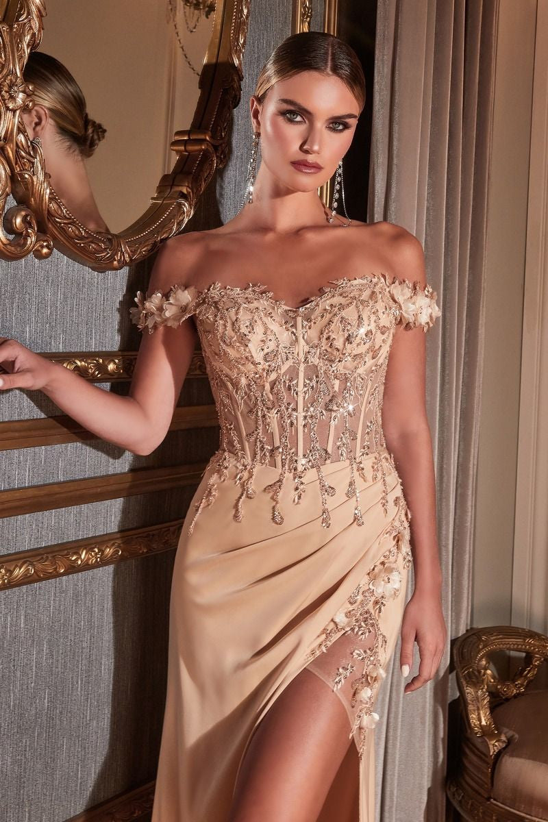 A woman in an elegant, off-the-shoulder gown adorned with intricate beading and floral details stands against an ornate mirror, radiating sophistication in a lavish, softly lit interior.