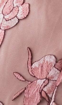 A detailed close-up of embroidered floral designs on soft, textured fabric. The delicate pink flowers and leaves are intricately stitched against a muted background, enhancing the elegance of the textile.