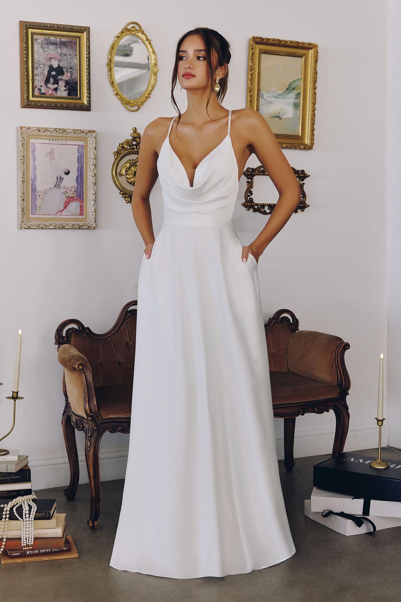 Woman in a white dress standing in an elegant room with decorative furniture and wall art.