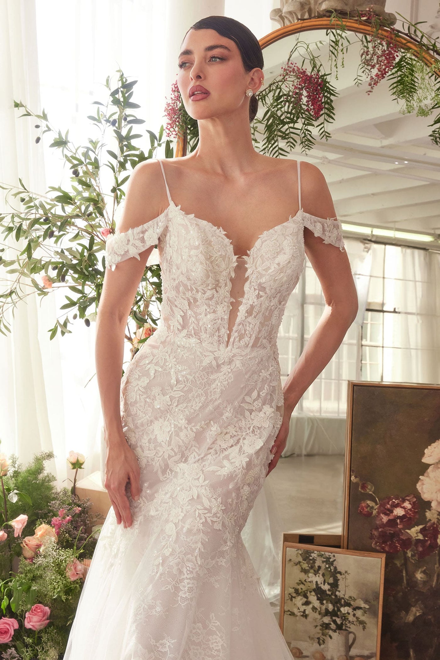 Woman wearing a white lace wedding dress in a decorated room with flowers and mirrors.