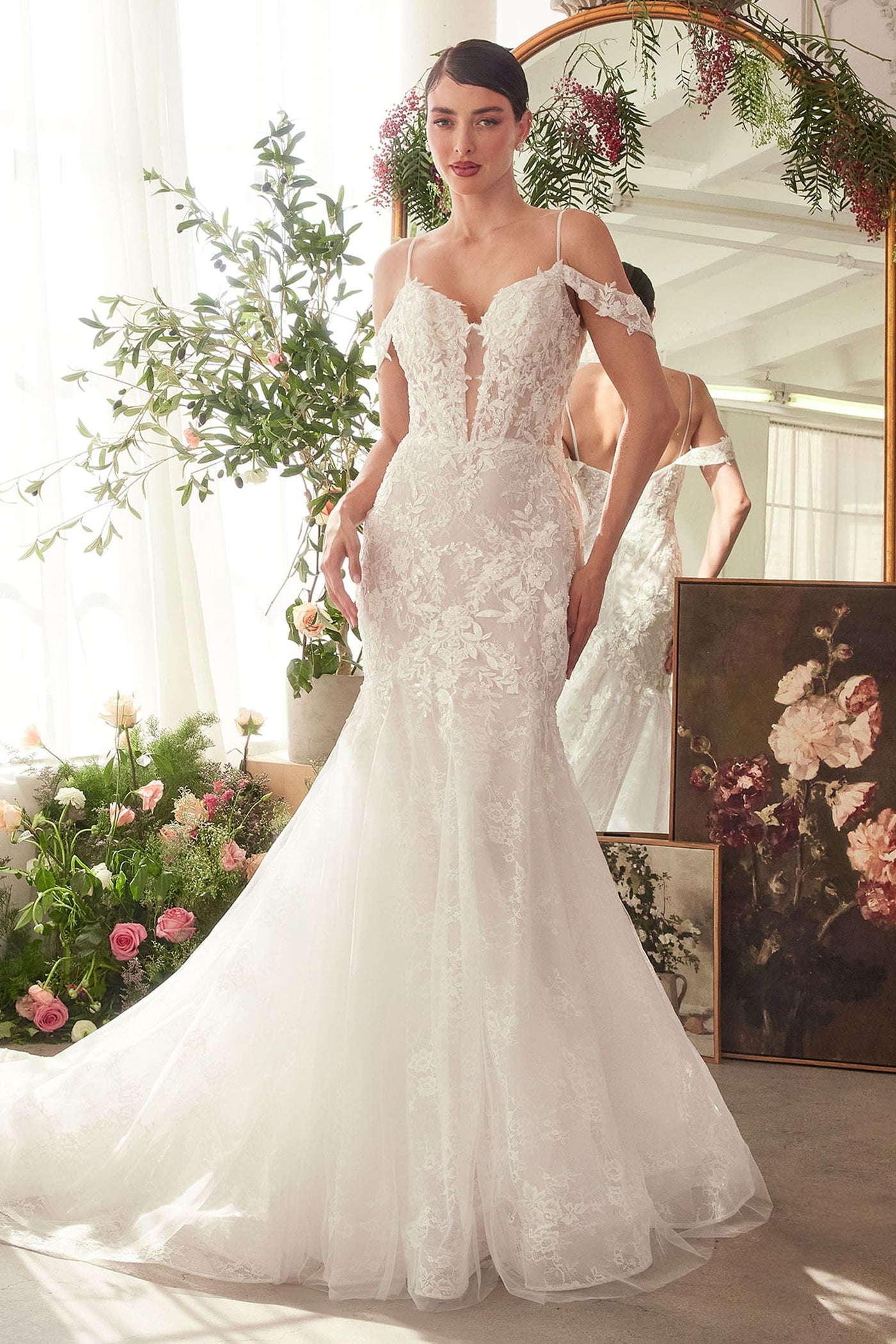 Woman in a white wedding dress standing in a decorated room with flowers and mirrors.