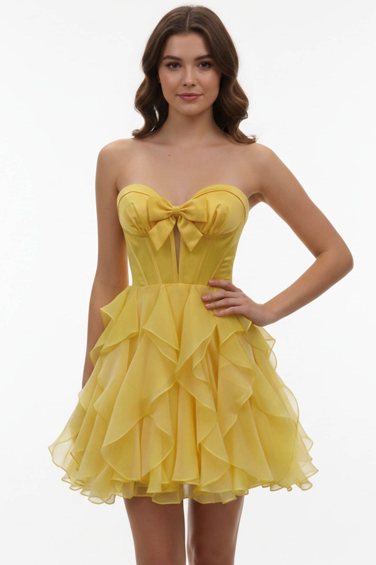 A woman modeling a bright yellow strapless mini dress with a sweetheart neckline, large bow at the bust, and a layered ruffled tulle skirt against a plain white studio background.