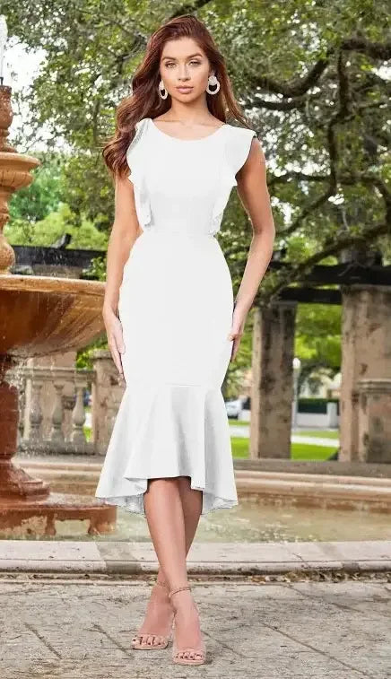 A woman in a fitted white dress with a flared hem stands confidently near a stone fountain, surrounded by greenery and soft lighting, creating a serene outdoor setting.