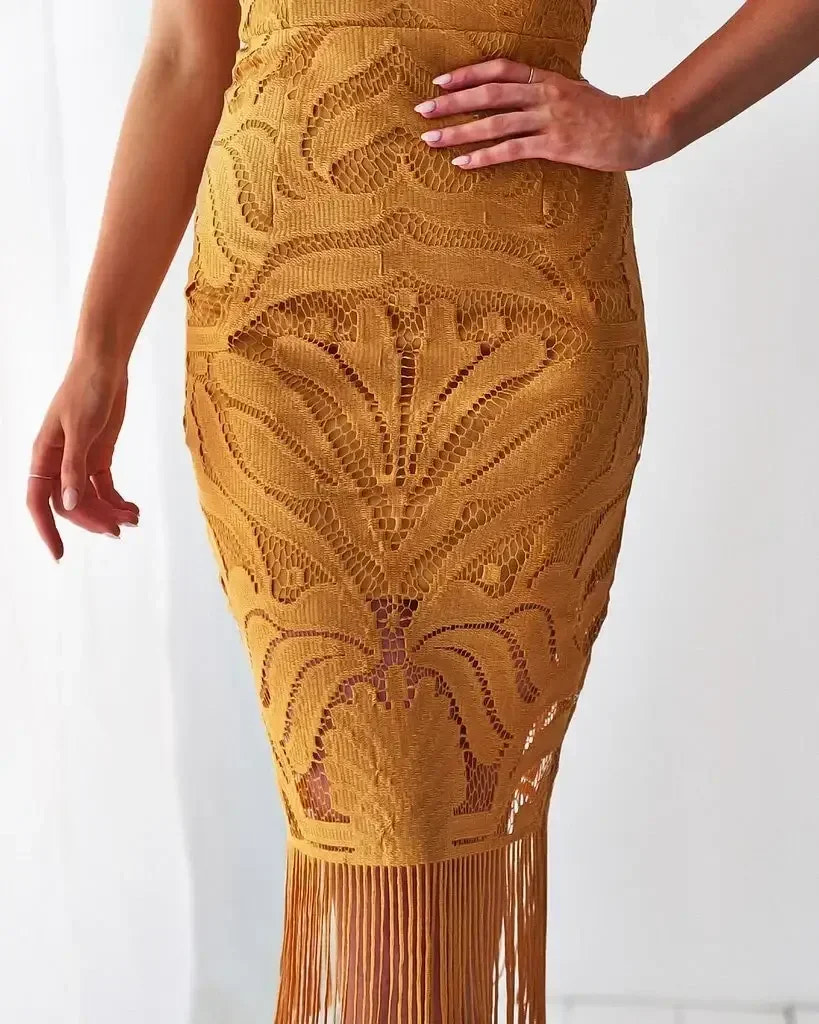 A lace skirt in a warm orange hue features intricate floral patterns and a fringed hem. A hand gently touches the skirt, set against a light, softly lit background.