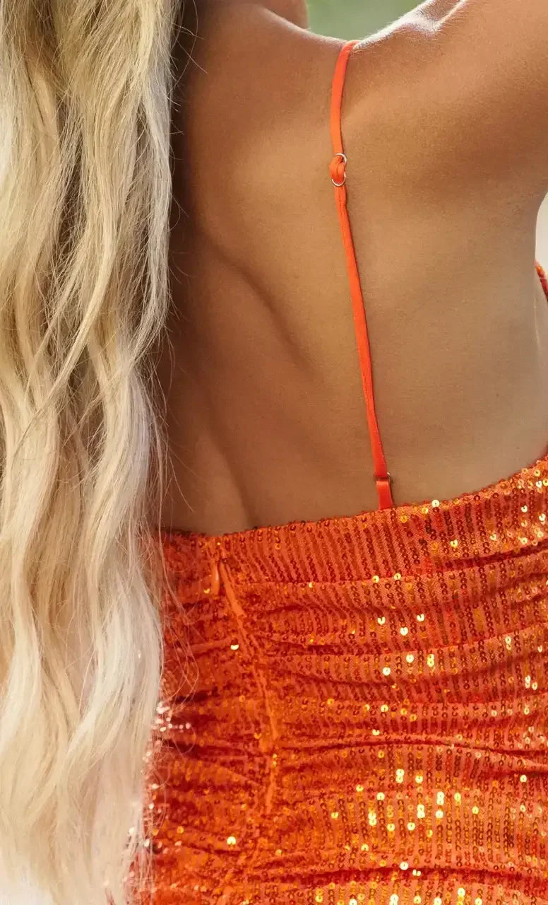 A person is wearing an orange, sequined dress that fits snugly, with one shoulder strap visible. Long, wavy blonde hair cascades down alongside their back, suggesting a stylish, vibrant setting.