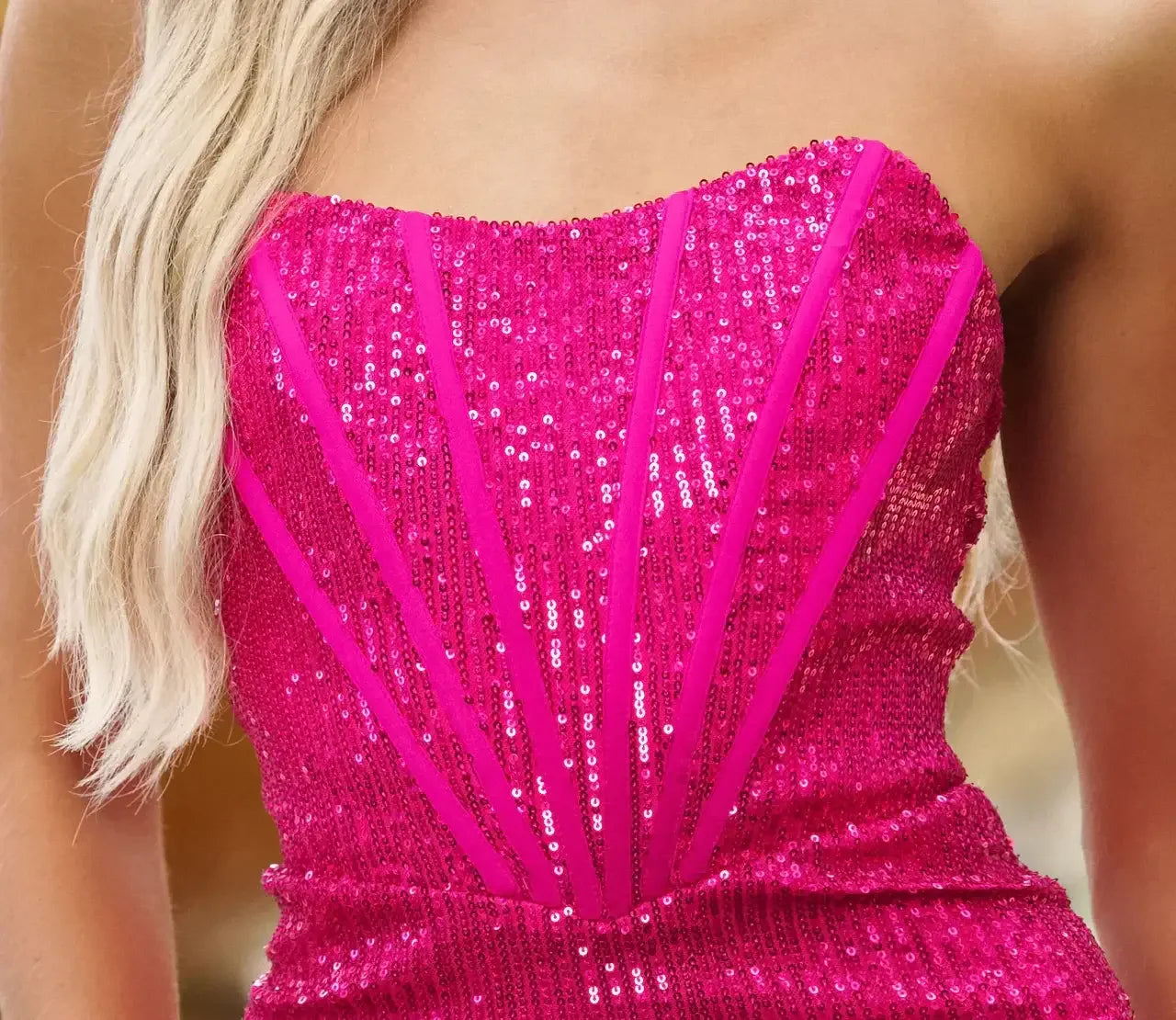 A vibrant pink sequin dress features a strapless design with angular lines. Its shimmering surface catches light, suggesting a festive or elegant context, possibly for an event or celebration.
