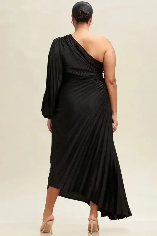 A flowing black dress with one shoulder and pleated fabric drapes elegantly over the figure, set against a neutral, light background. The style conveys sophistication and modernity.