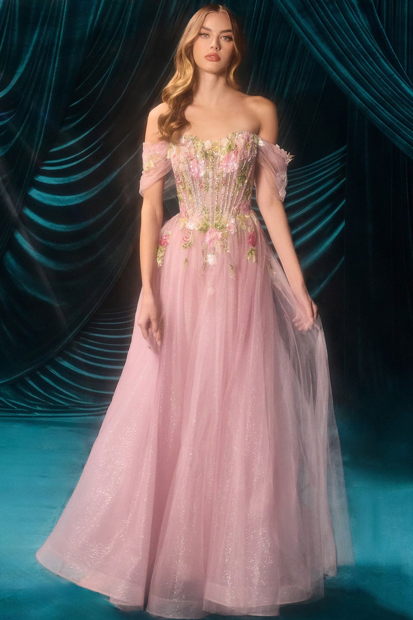 Woman in a pink floral gown standing against a dark, textured curtain.