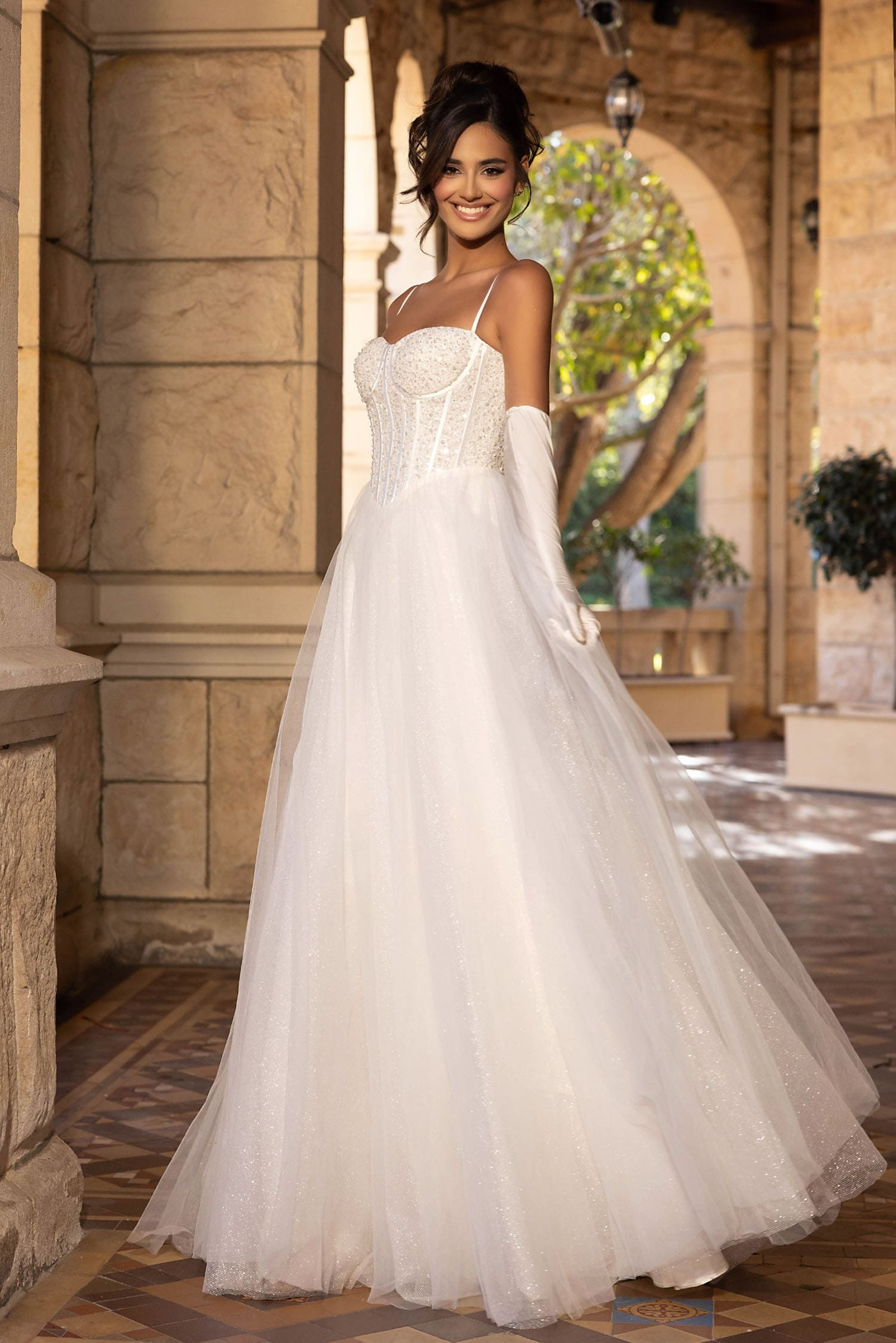 Woman in a white wedding dress standing in an outdoor setting with stone architecture.