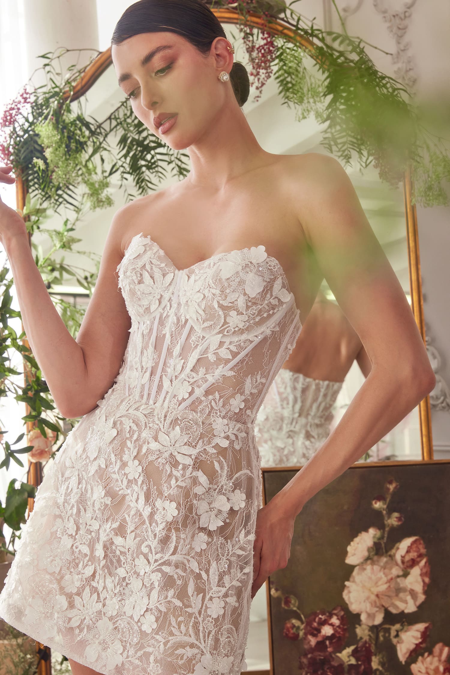 Woman wearing a white lace dress with floral decorations in a softly blurred indoor setting.