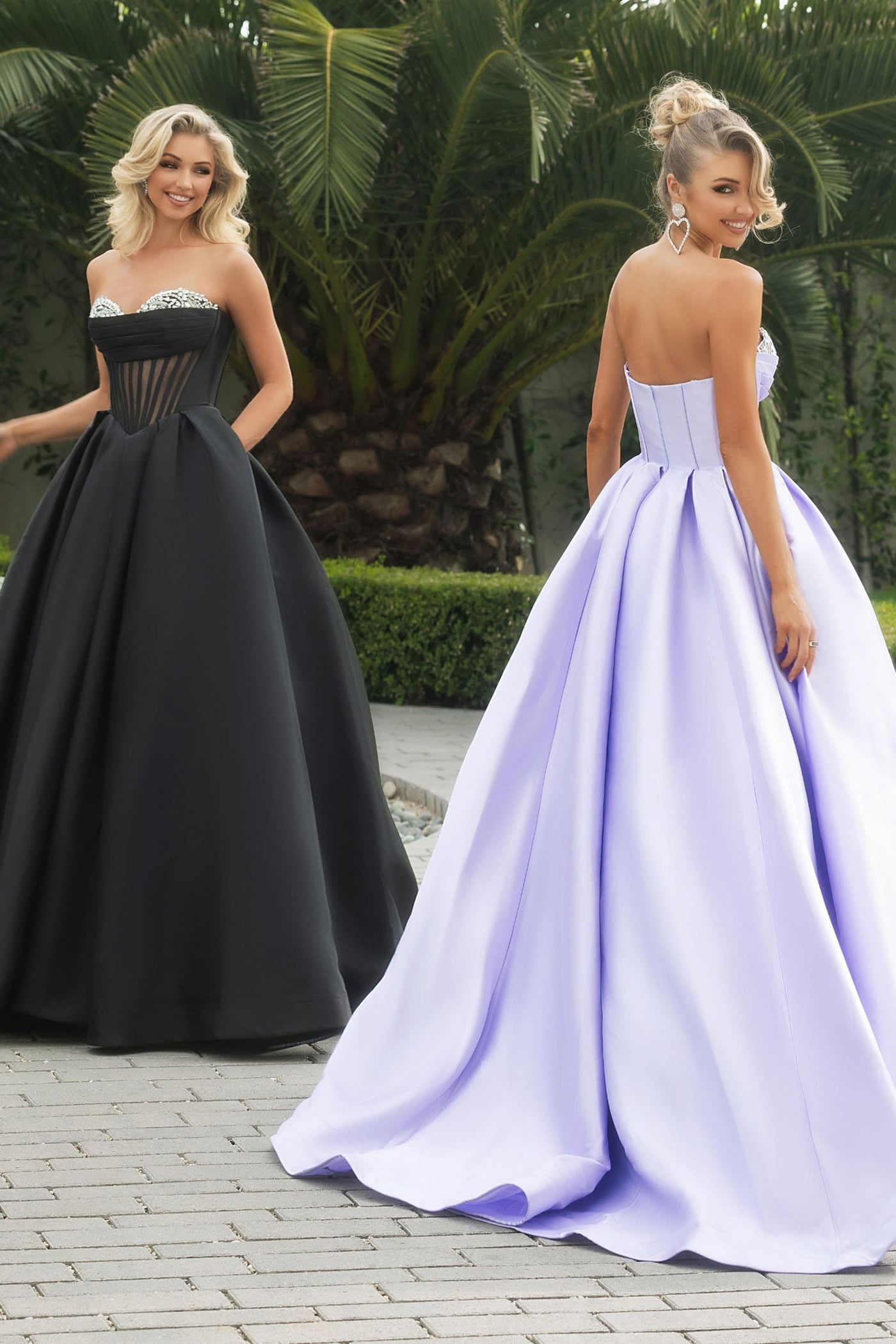 Two women in formal dresses standing outdoors with greenery in the background