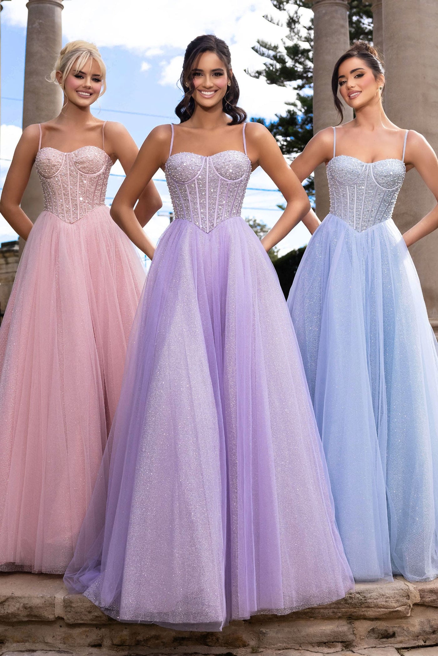 Three women wearing pastel-colored evening gowns standing outdoors.