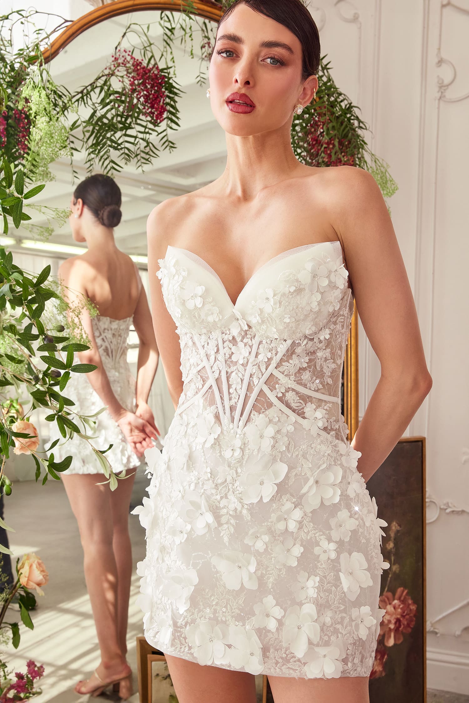 Woman wearing a white floral dress standing in a decorated room with plants.