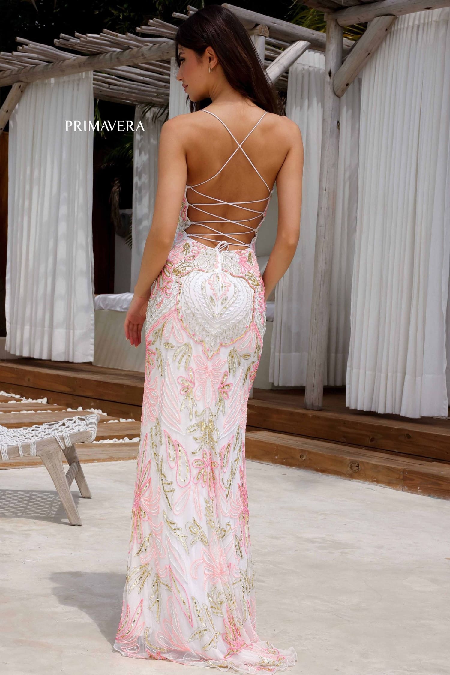 Woman wearing a floral dress with a backless design, standing on a wooden deck with white curtains in the background.
