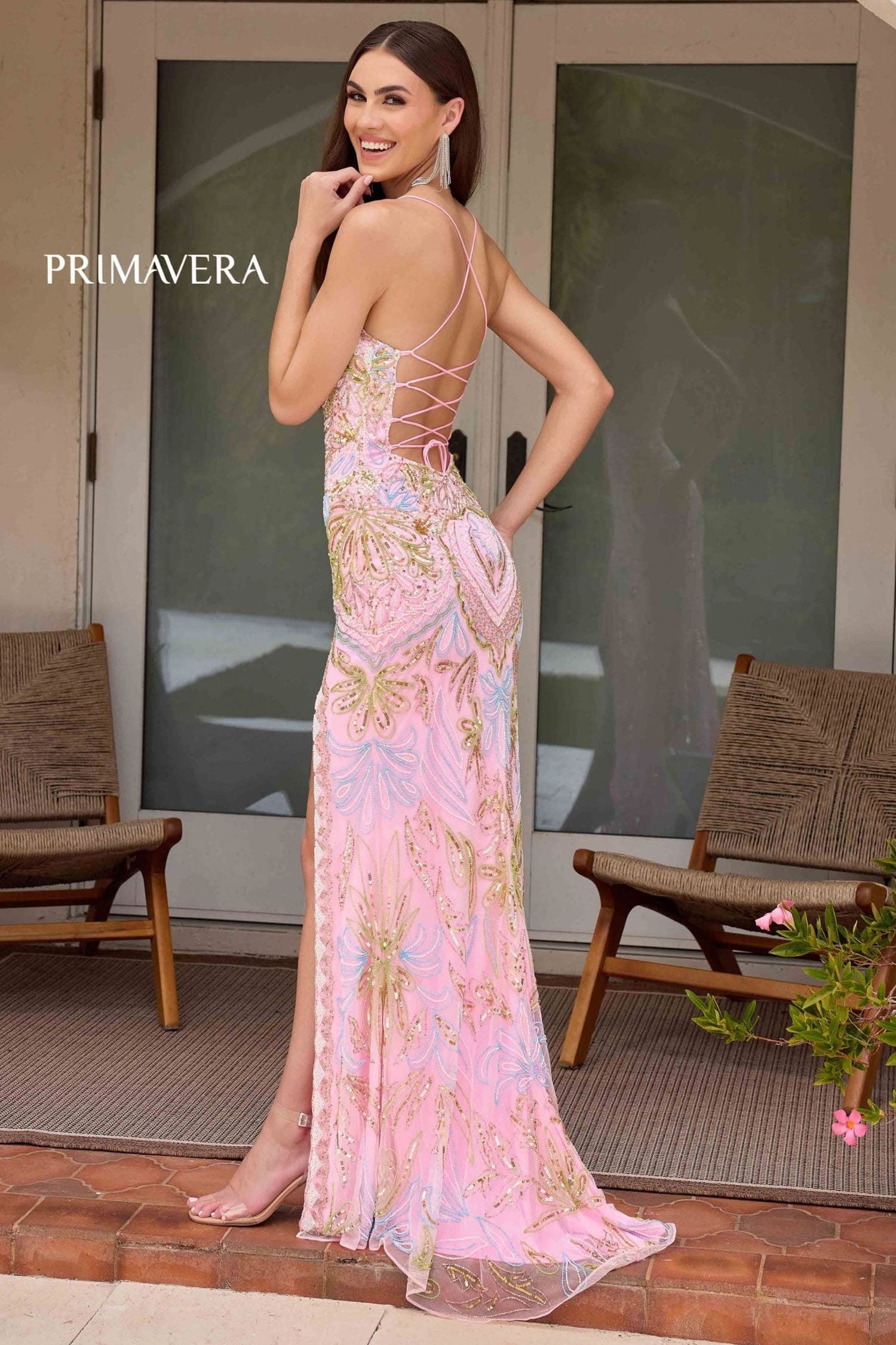 Woman wearing a pink floral dress with 'PRIMAVERA' branding, standing outdoors.