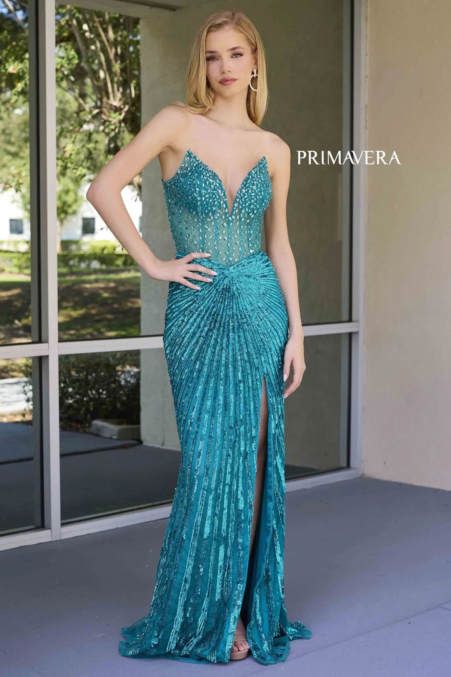 Woman wearing a teal evening gown with a high slit, standing indoors.