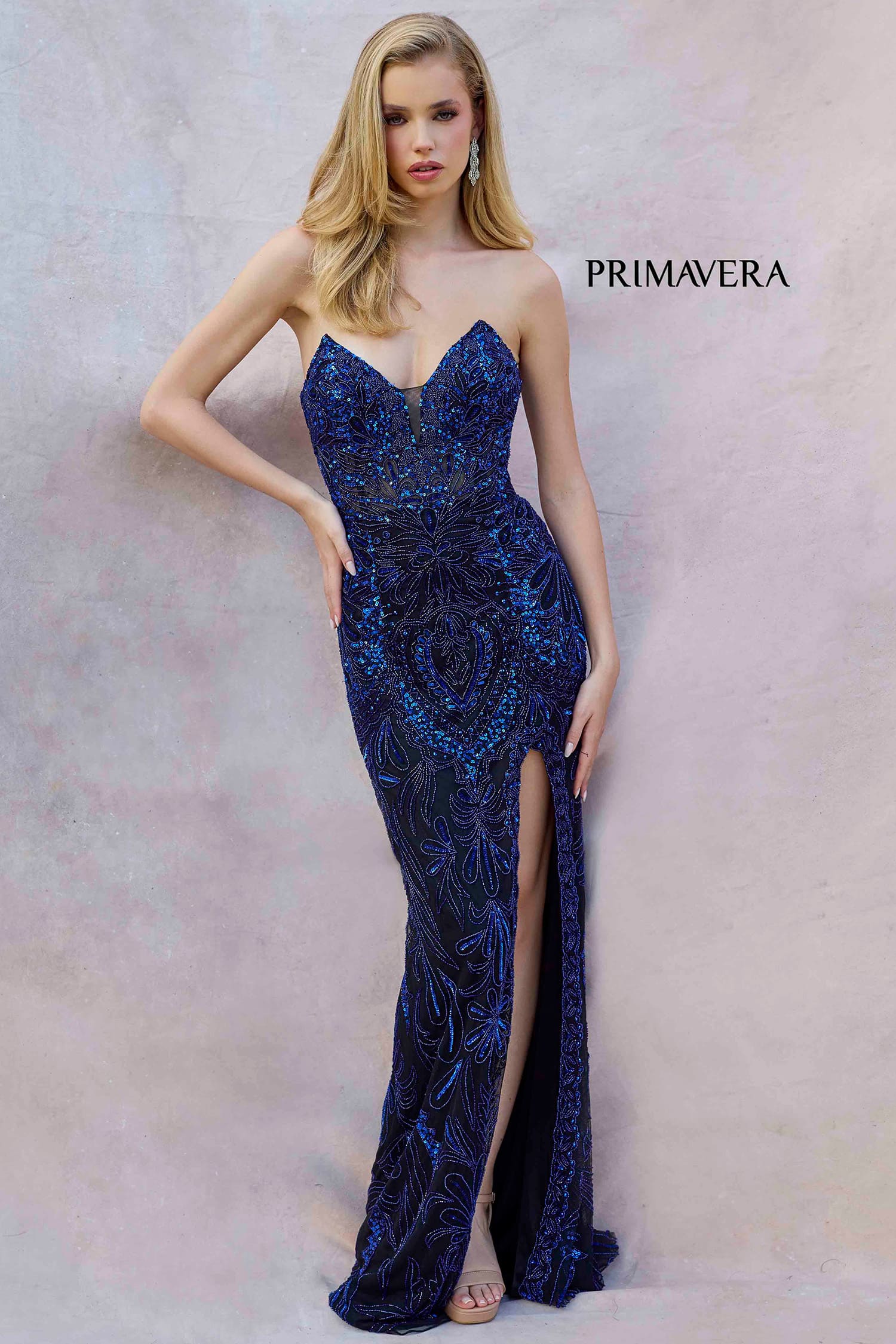 Woman wearing a blue sequin evening gown with a slit on a plain background, branded 'Primavera'.