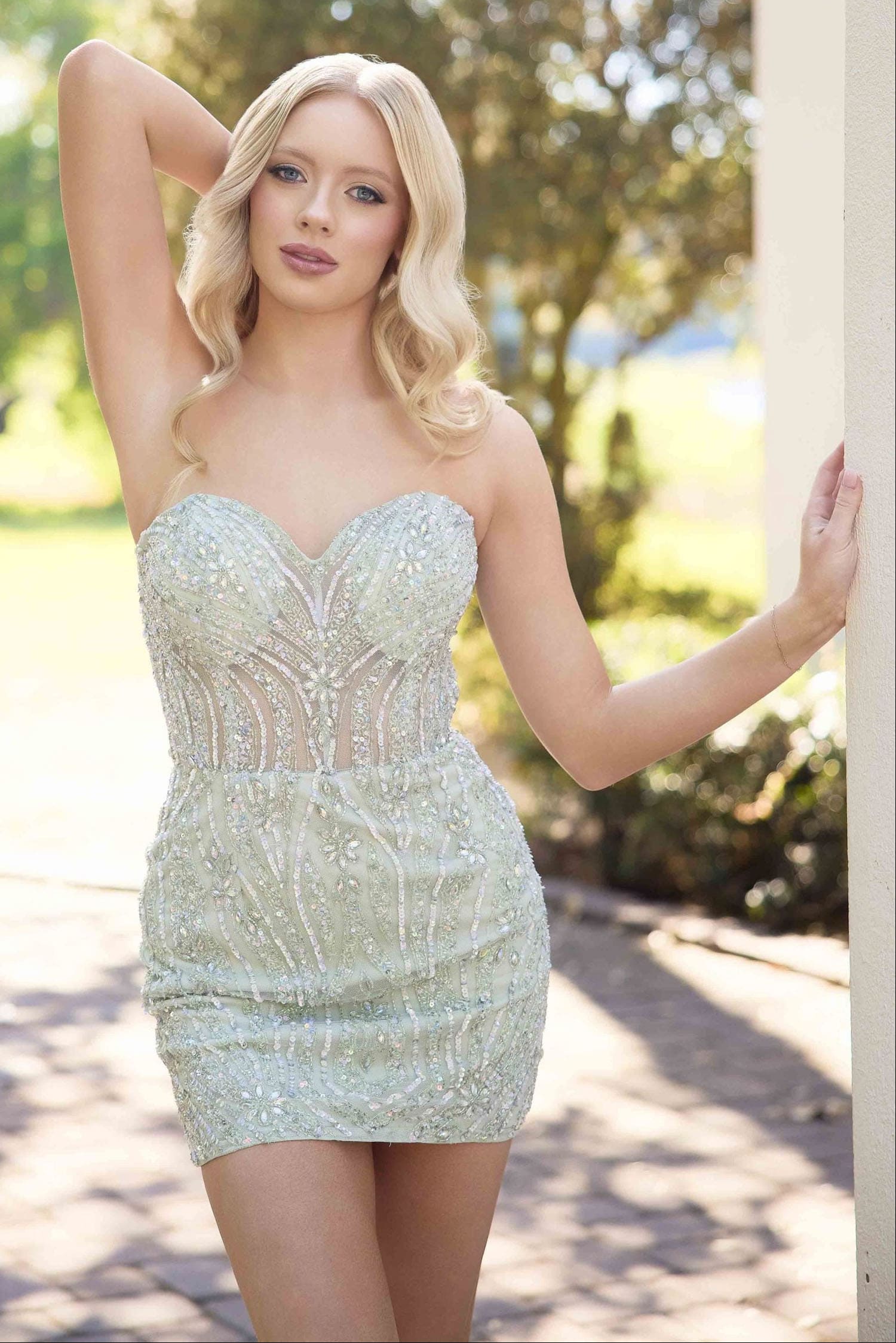 Woman in a strapless, light-colored dress standing outdoors with trees in the background
