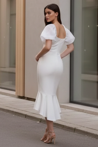 Woman in a white dress standing on a street in front of a modern building.