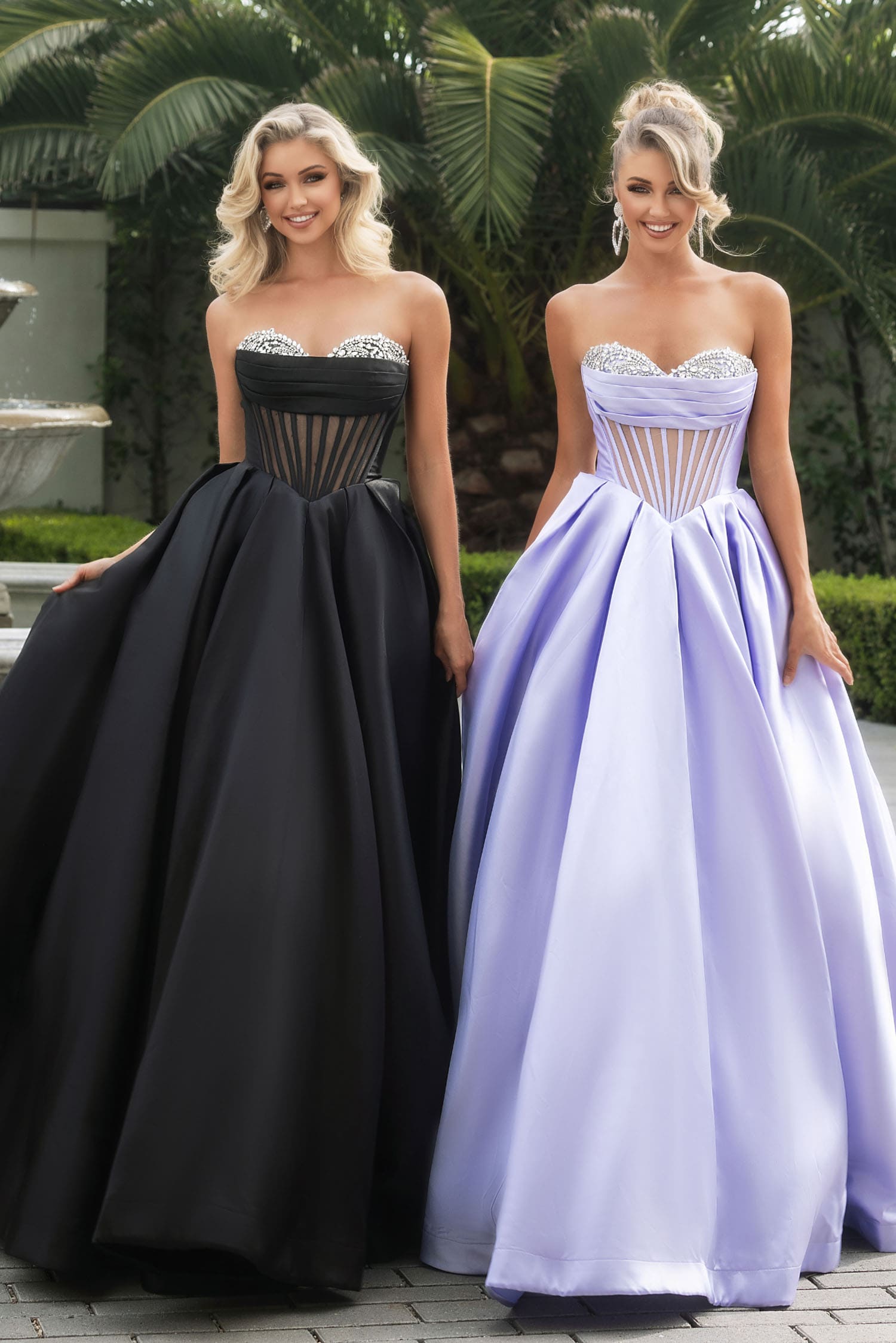 Two women wearing strapless evening gowns, one black and one lavender, standing outdoors.