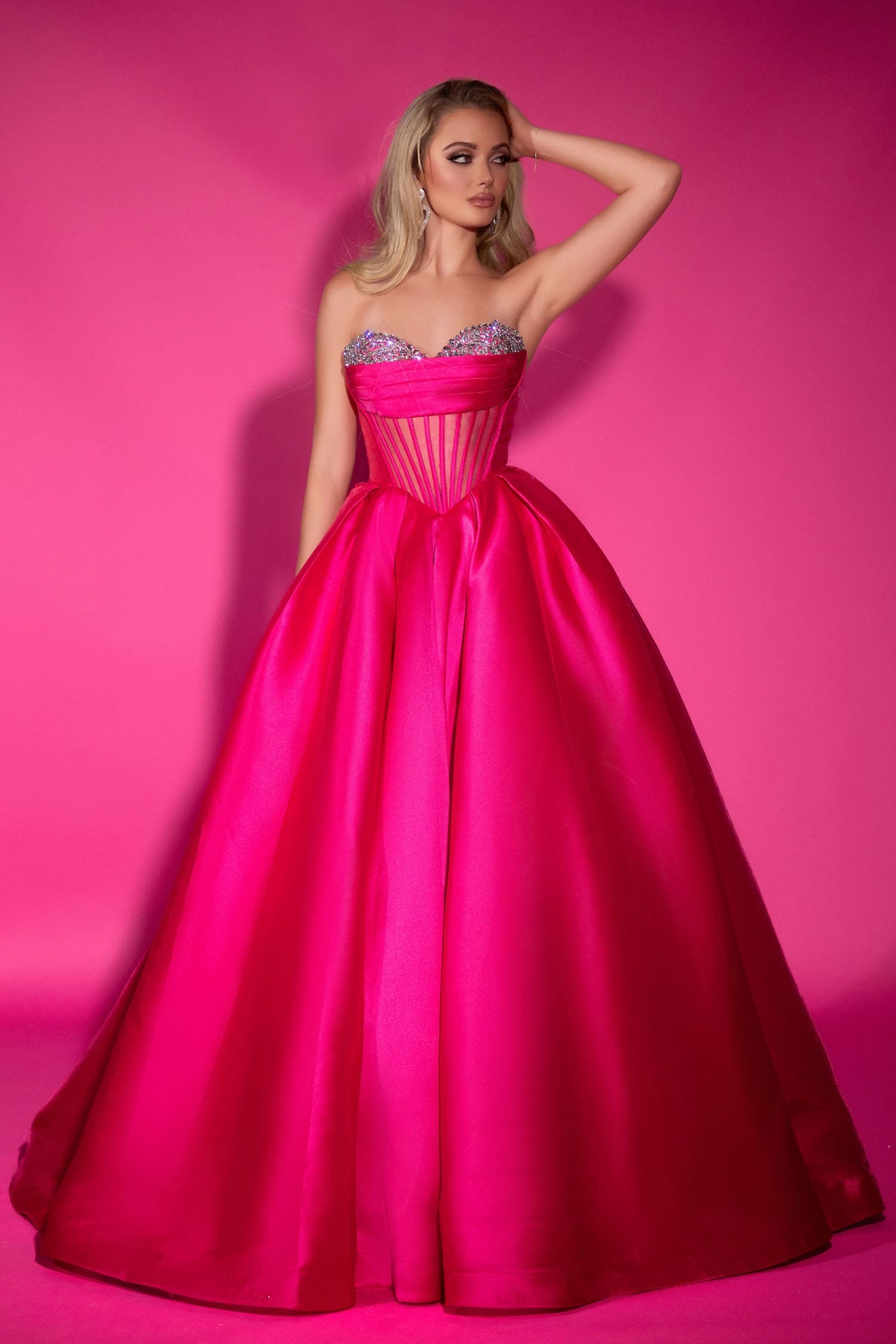 Woman in a pink gown with a sparkly bodice against a pink background