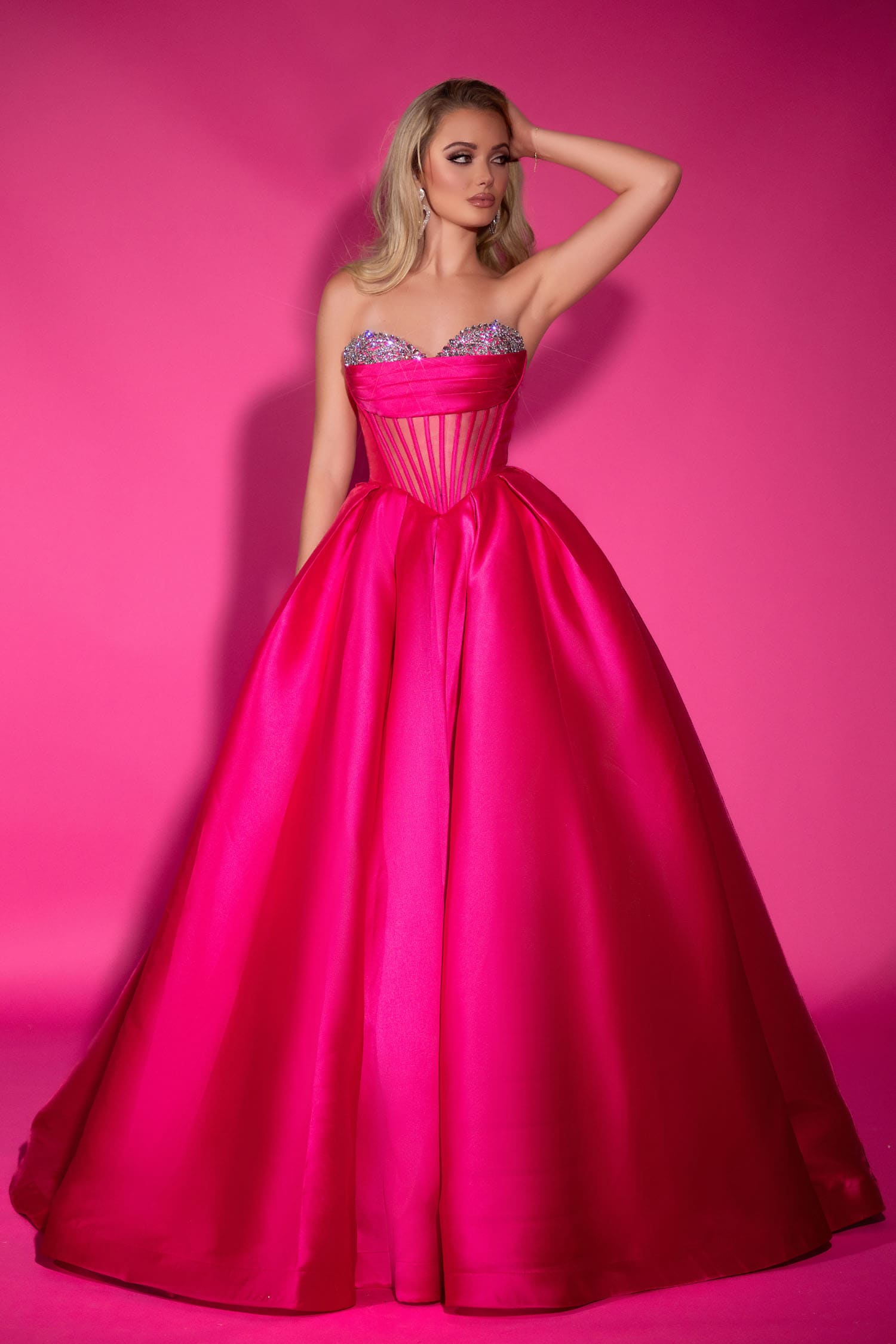 Woman in a pink gown with a sparkly bodice against a pink background