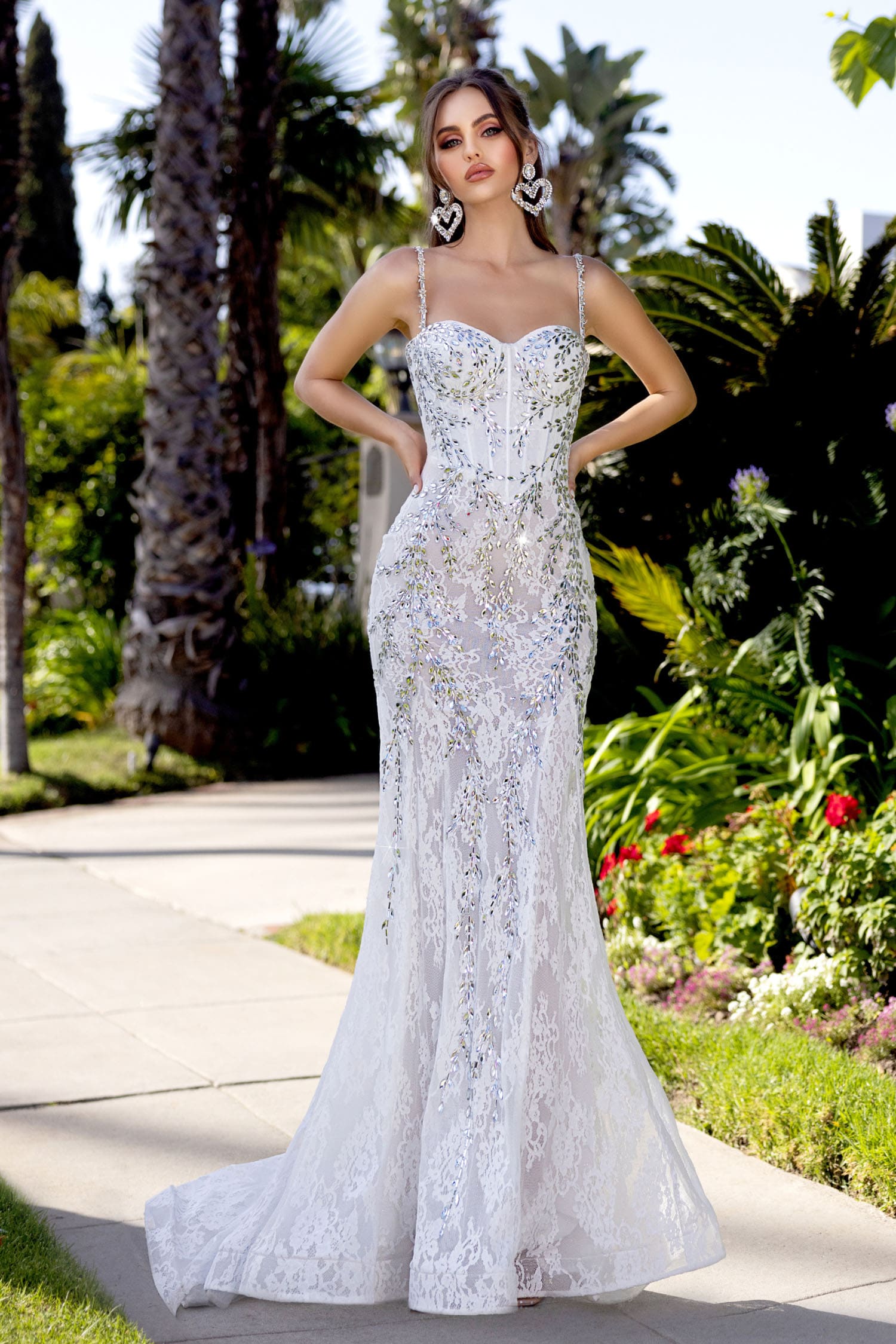 Woman in a white lace evening gown standing outdoors with greenery in the background