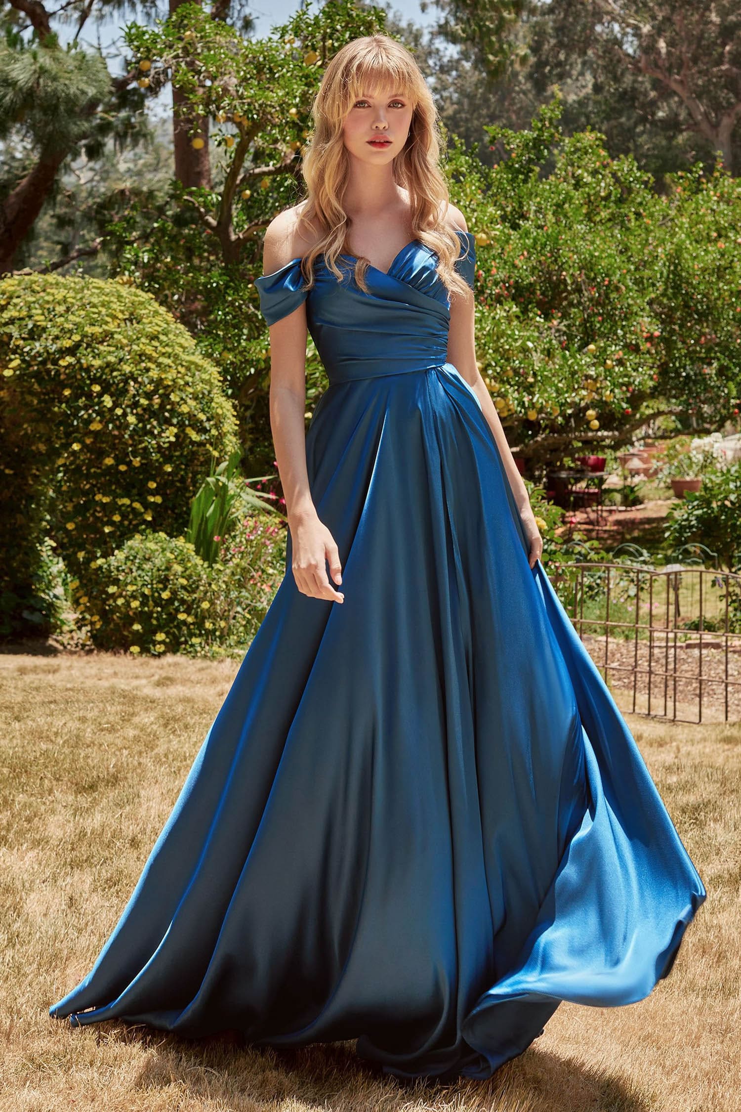 Woman in a blue evening gown standing outdoors in a garden setting
