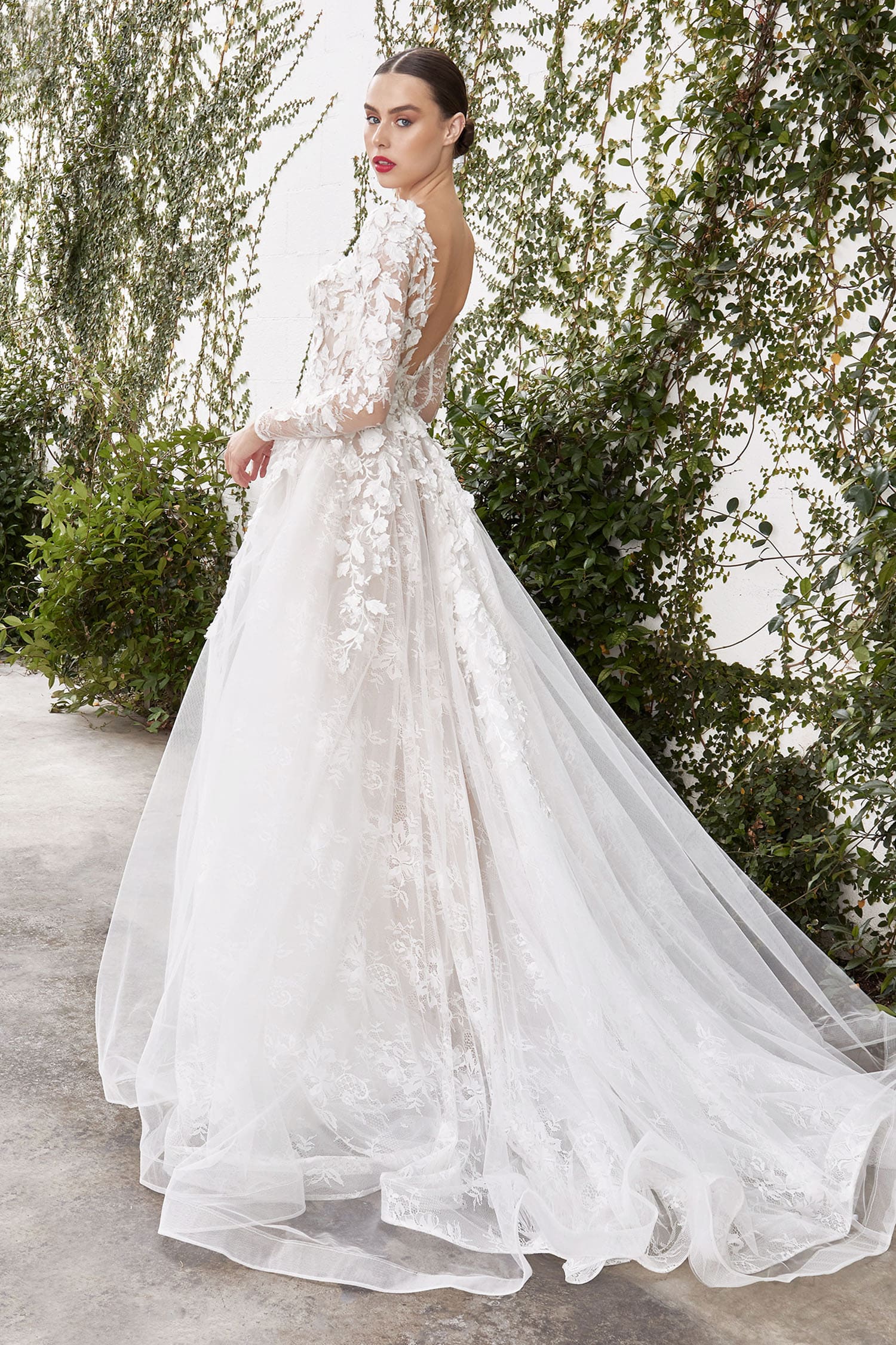 Woman in a white floral wedding dress standing outdoors with greenery in the background