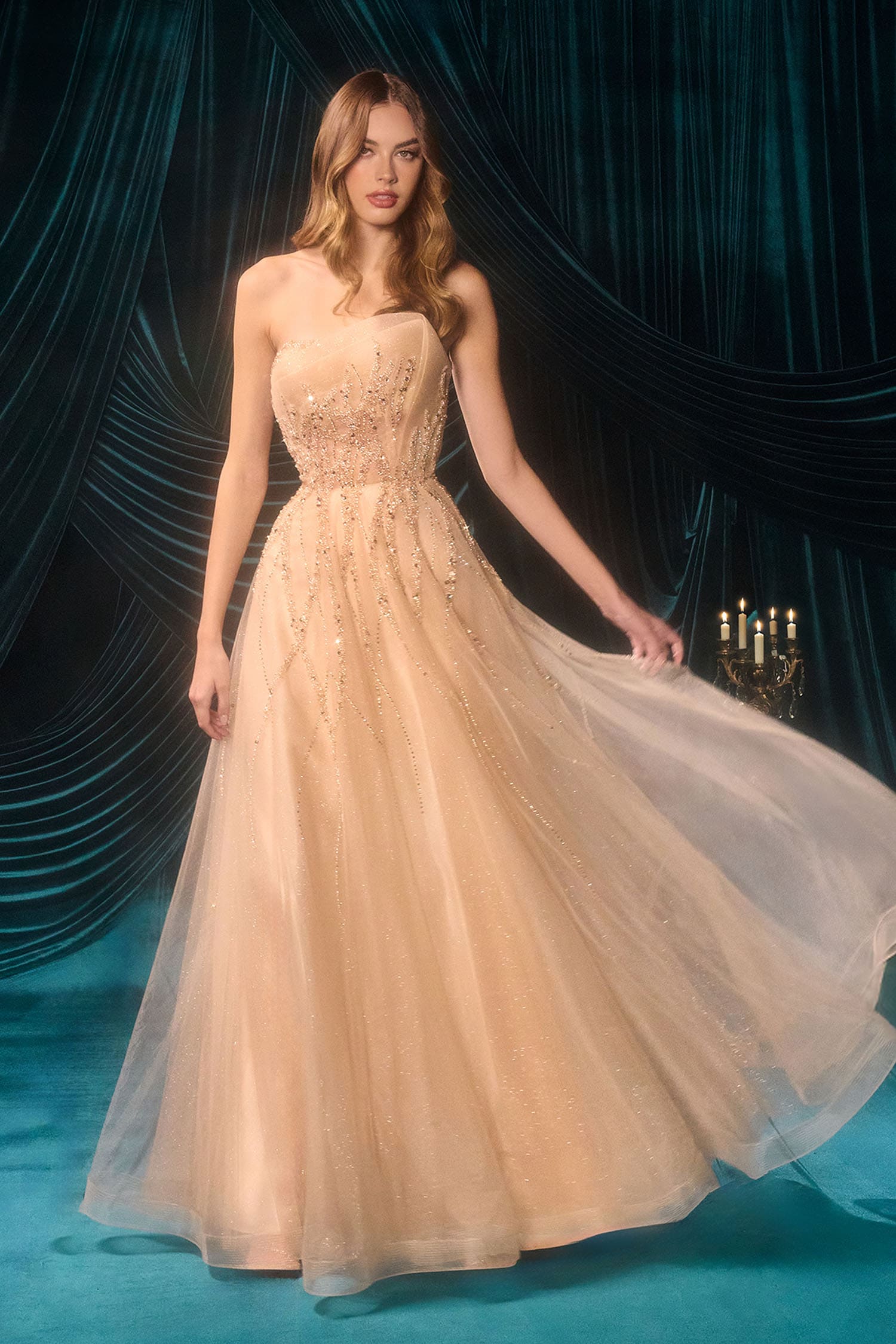Woman in a beige evening gown against a dark, decorative curtain background