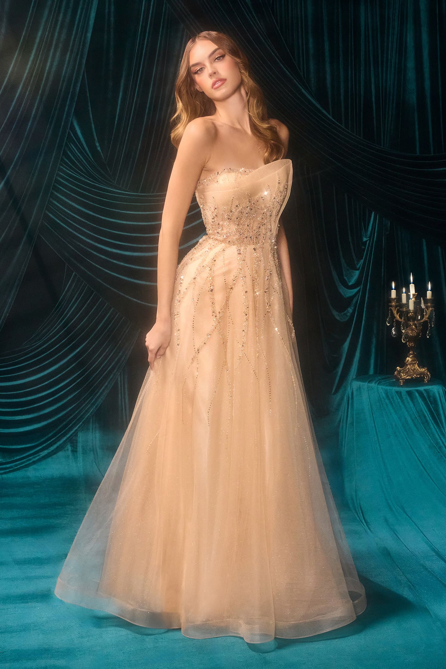 Woman in a beige evening gown with intricate detailing against a blue curtain backdrop