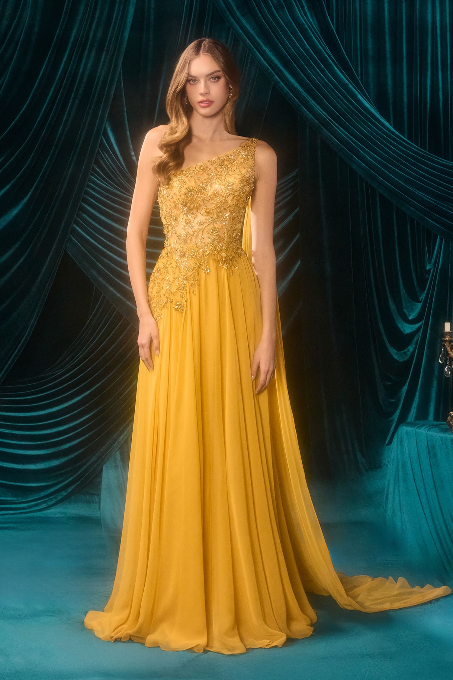 Woman in a yellow evening gown standing against a blue curtain backdrop