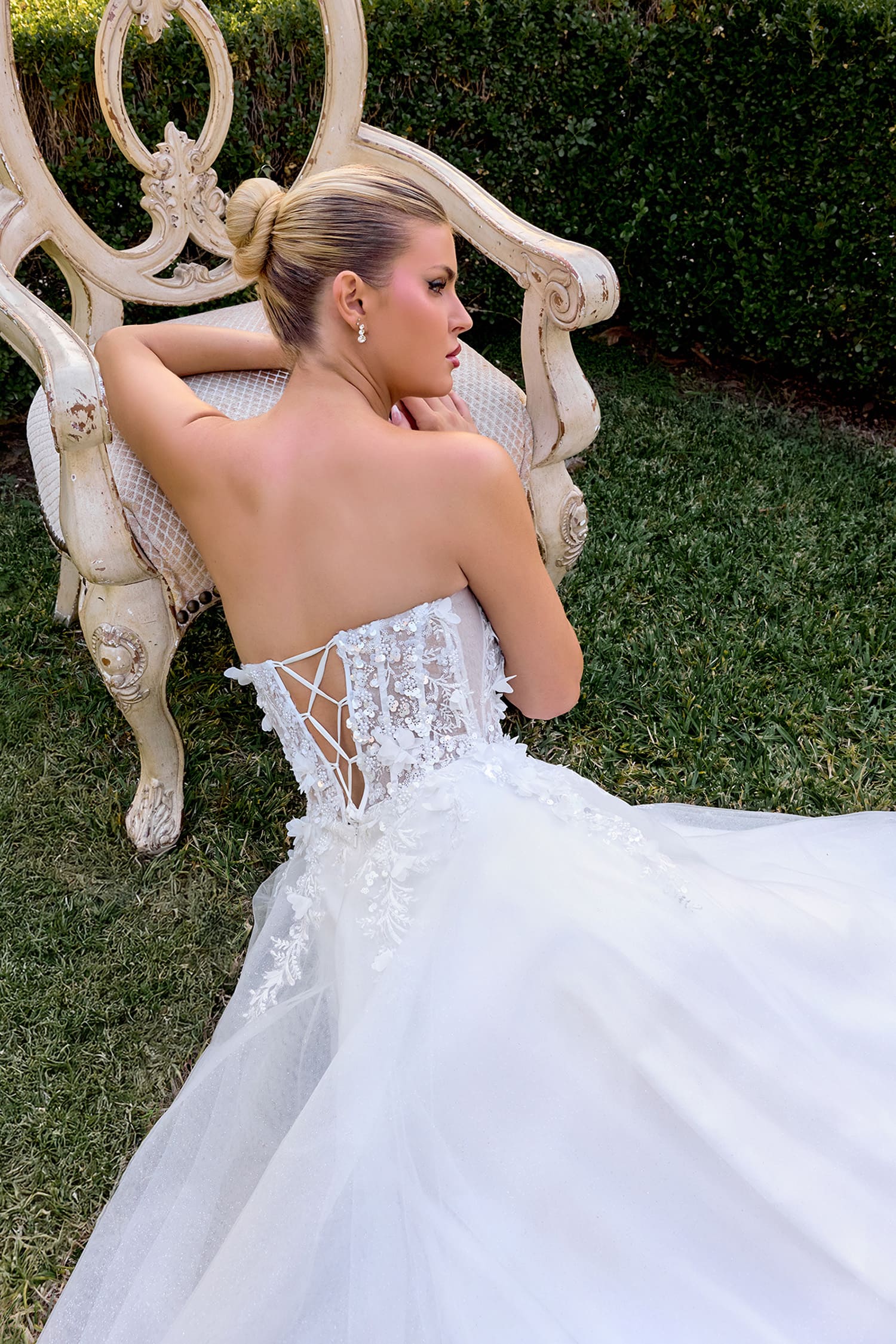 Woman in a white wedding dress sitting on an ornate chair outdoors.