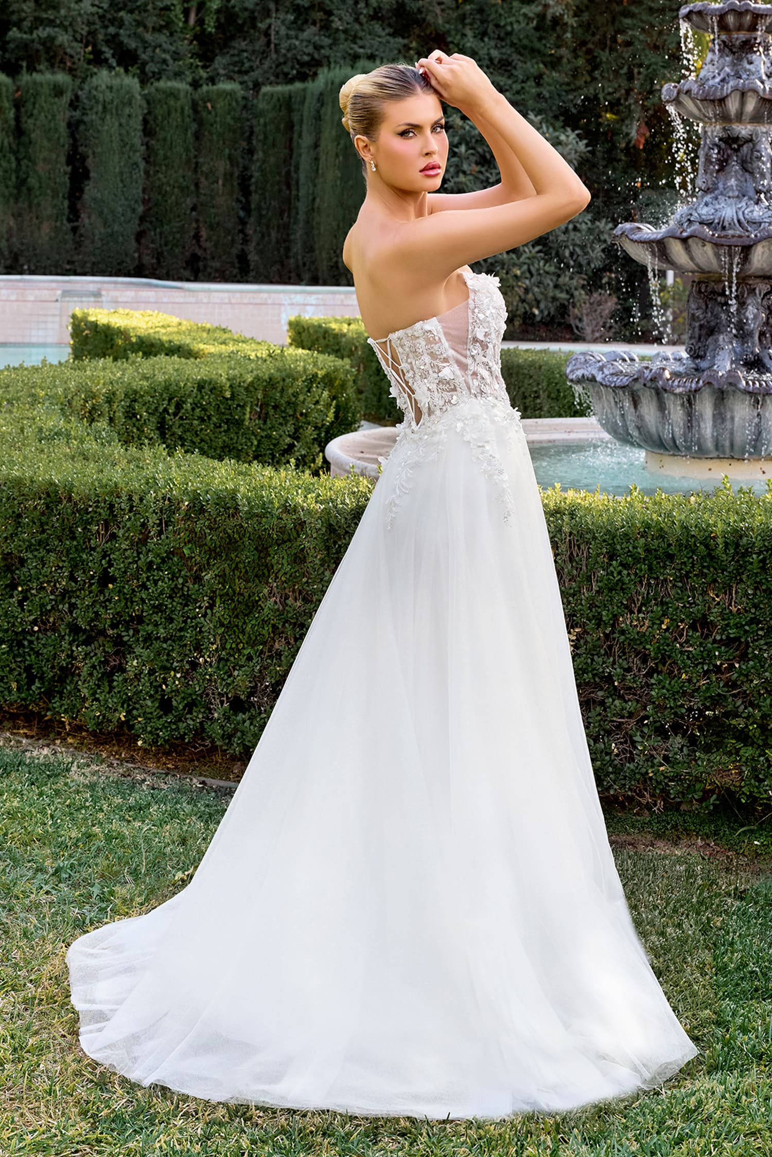 Woman in a white wedding dress standing in a garden with a fountain.