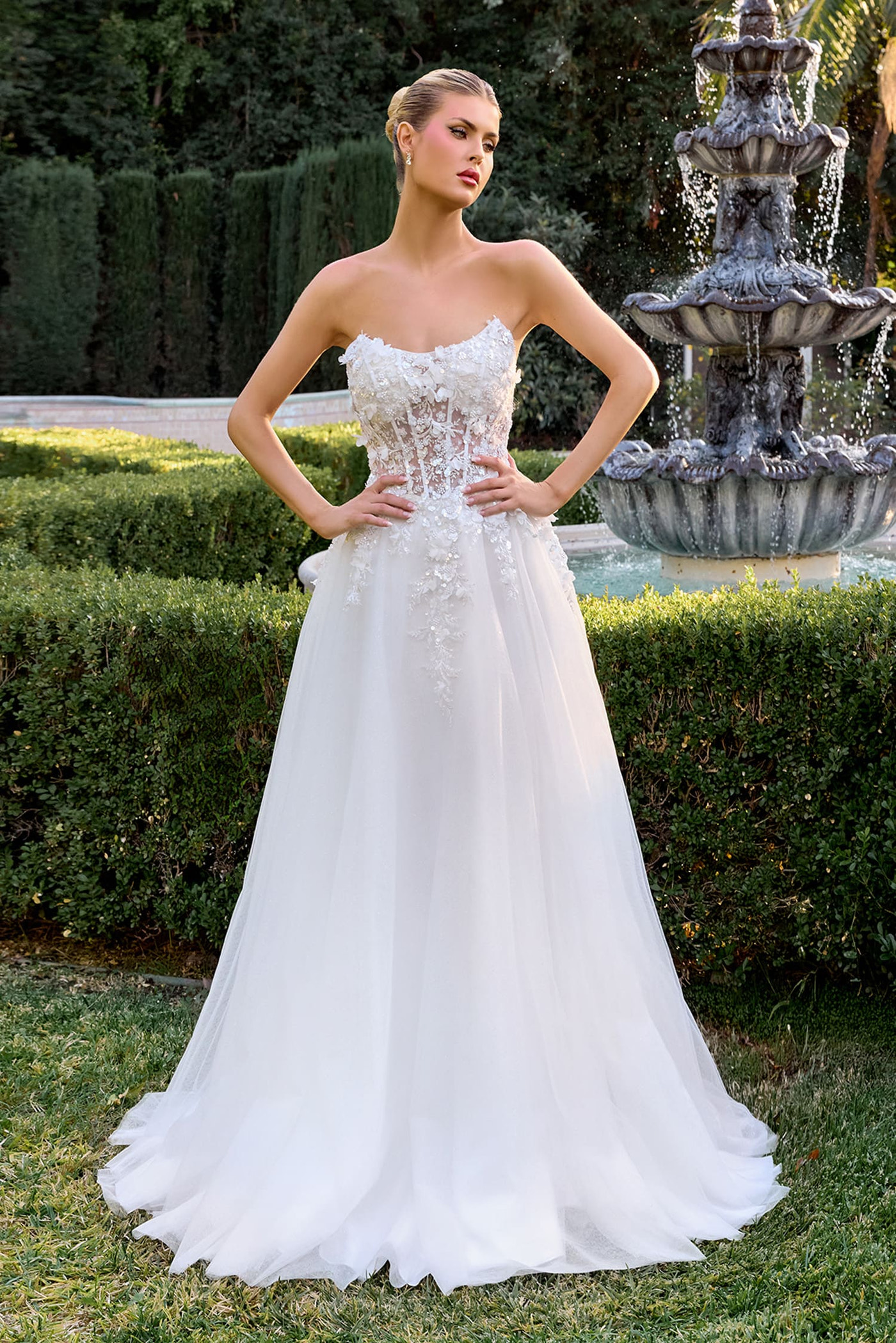 Woman in a white wedding dress standing in a garden with a fountain in the background