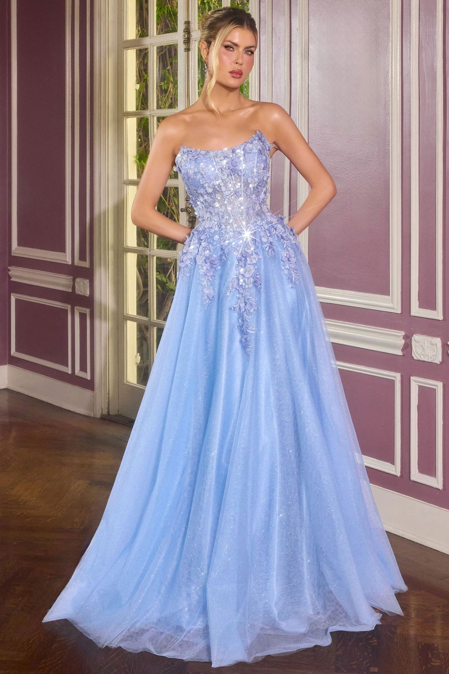 Woman wearing a light blue evening gown with intricate detailing in a room with decorative walls.
