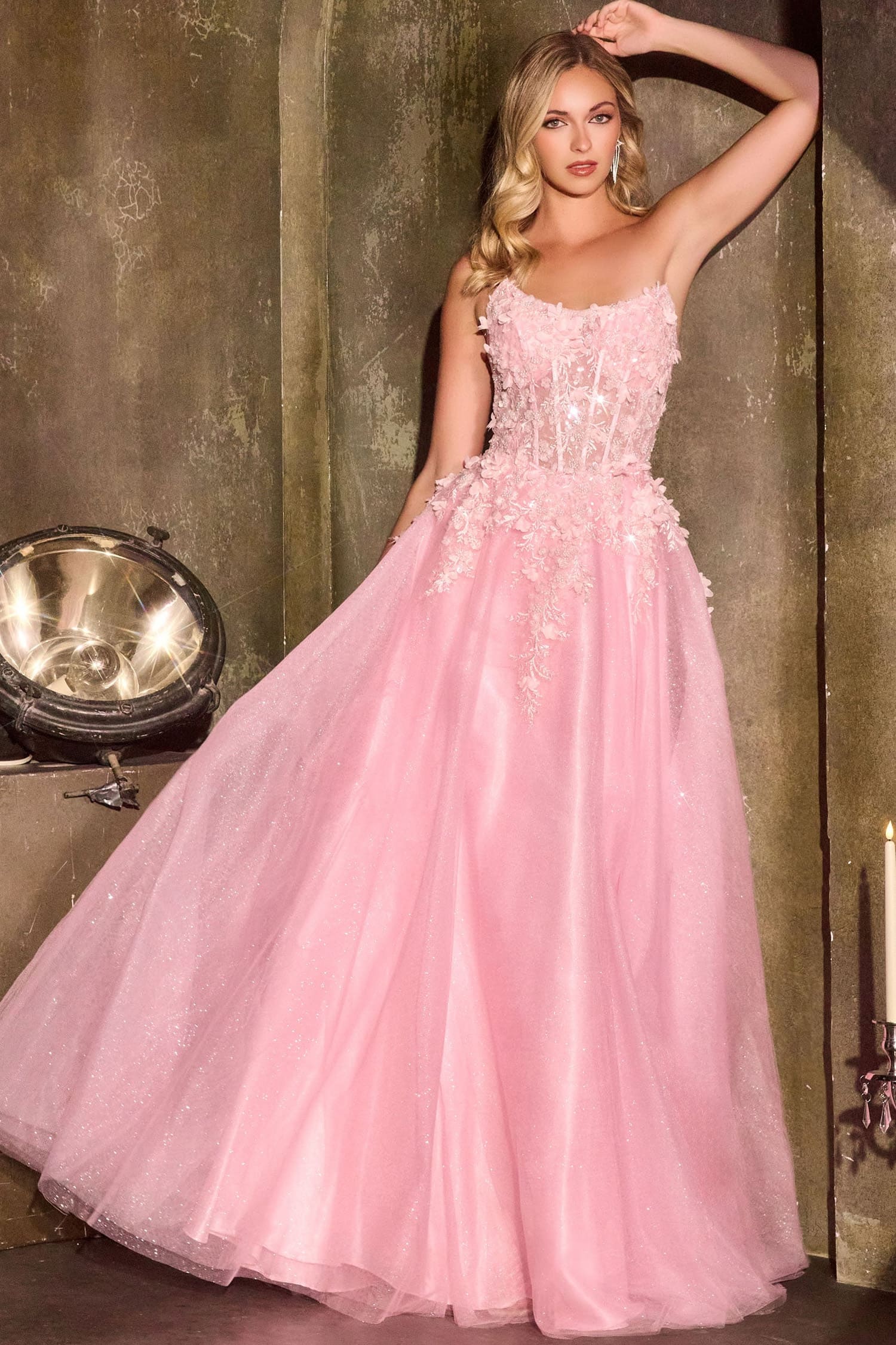 Woman in a pink evening gown standing against a textured wall.
