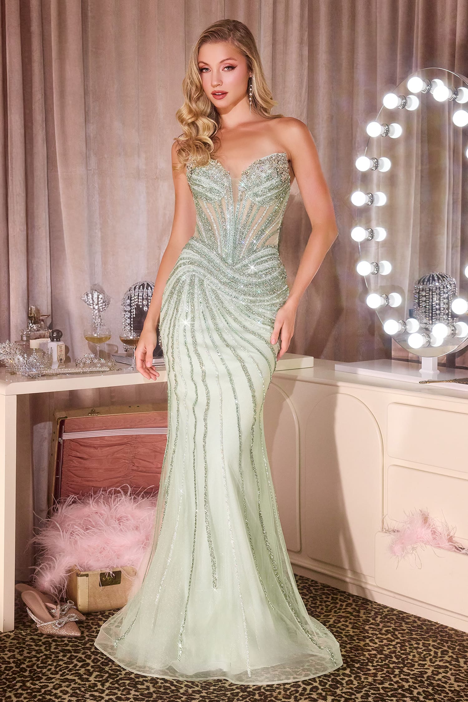 Woman in a light green evening gown standing in a room with vanity mirror and makeup.