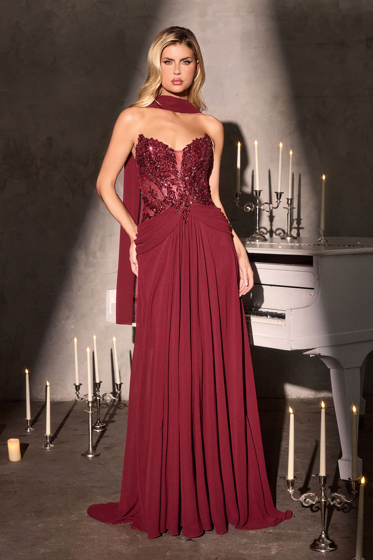 Woman in a burgundy evening gown standing in front of a piano with candles.
