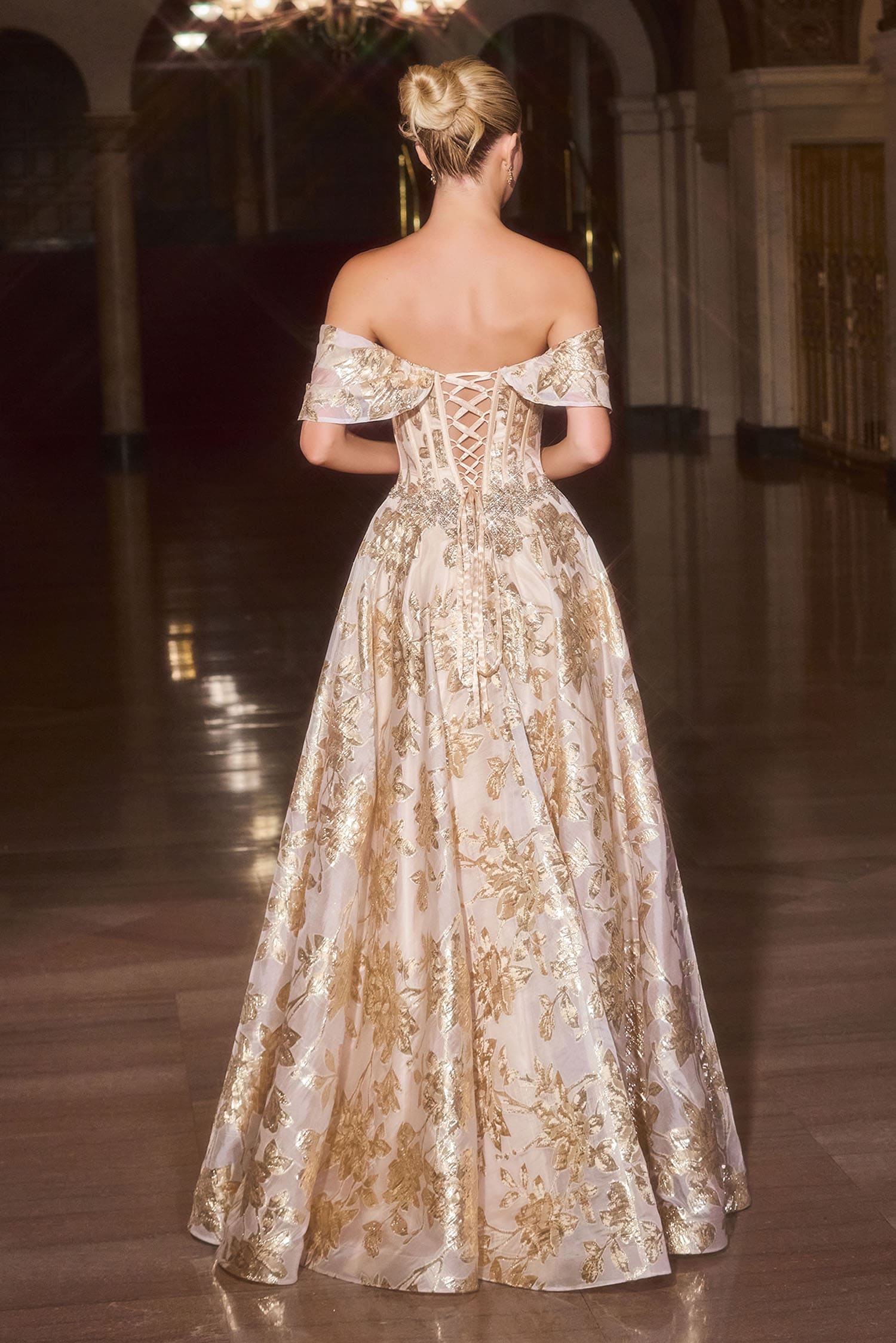 Woman in a gold evening gown with intricate detailing in an elegant indoor setting.