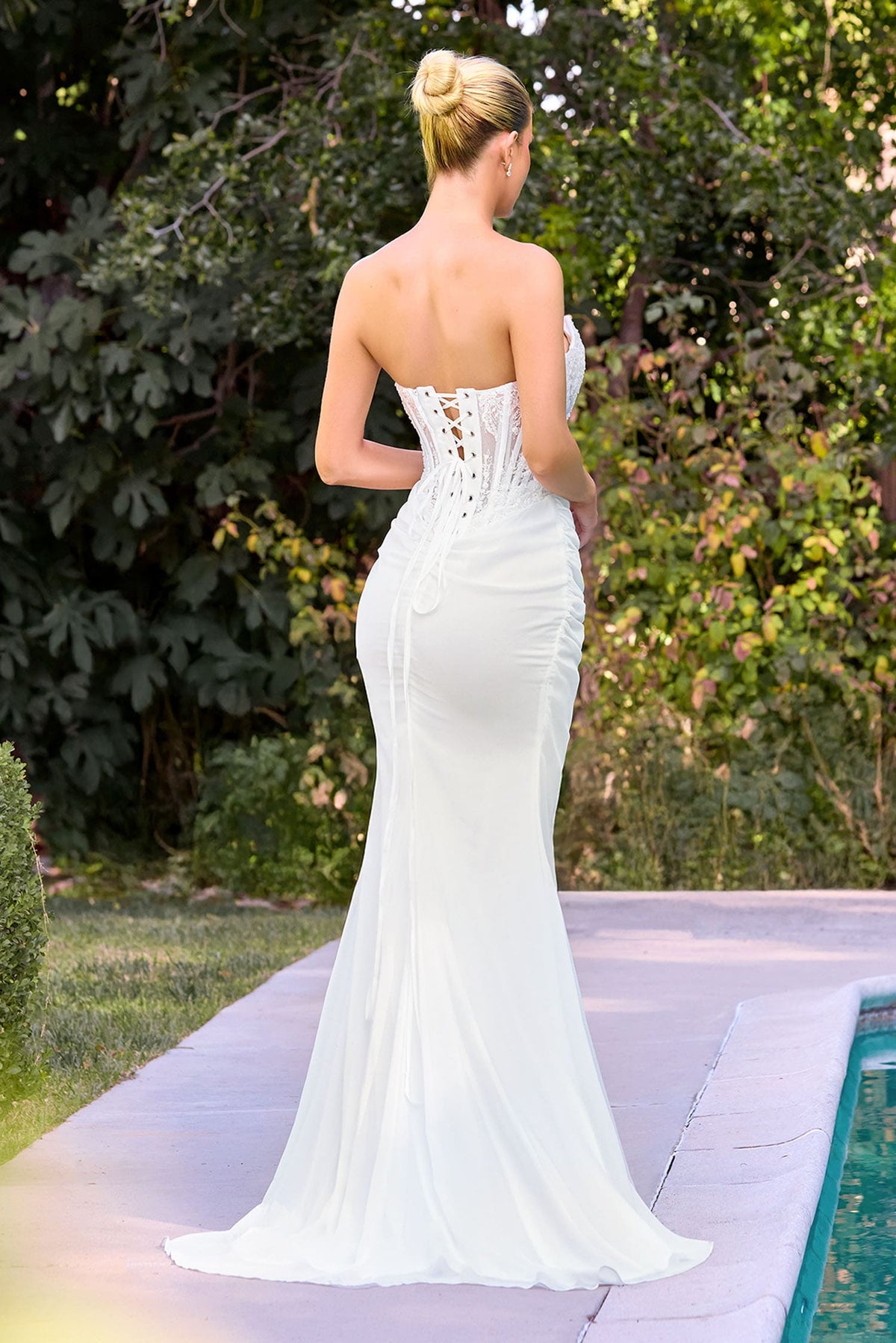 Woman in a white strapless gown standing outdoors with greenery in the background