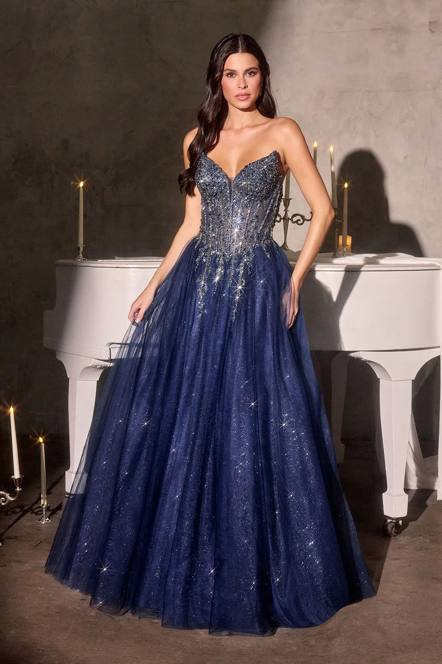 Woman in a sparkly blue evening gown standing in front of a white piano.