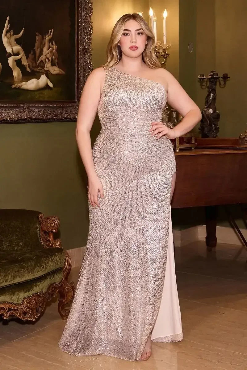 A woman stands confidently in a sparkling, one-shoulder gown. The elegant outfit contrasts with the vintage decor, including a dark painting and a wooden table, in a well-lit room.
