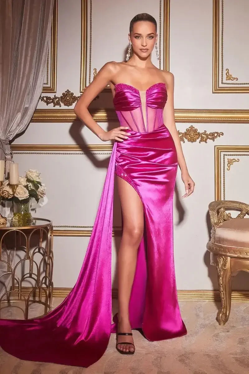 A woman stands confidently in a vibrant pink dress with a high slit, showcasing elegance in a lavish room adorned with gold accents, soft drapes, and floral decor.