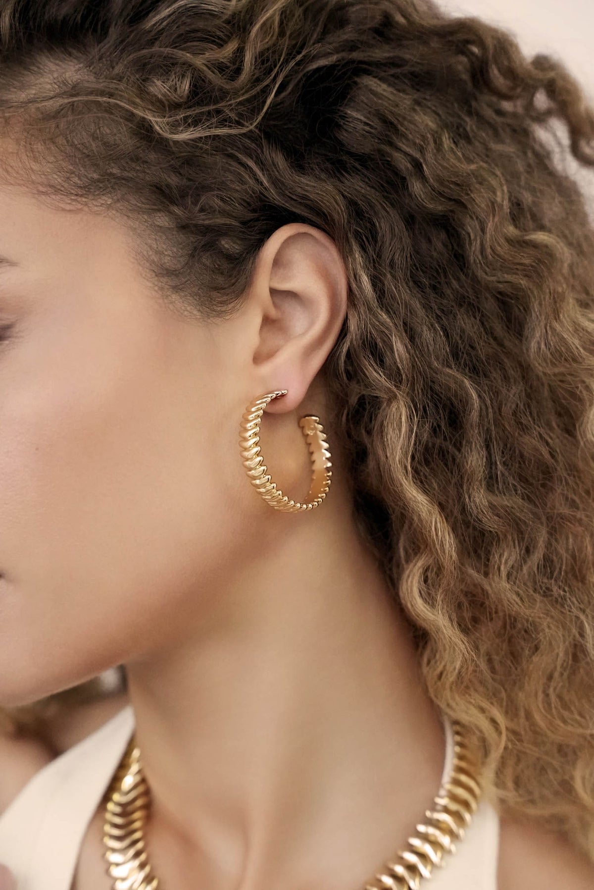Close-up of a person wearing gold hoop earrings with curly hair.